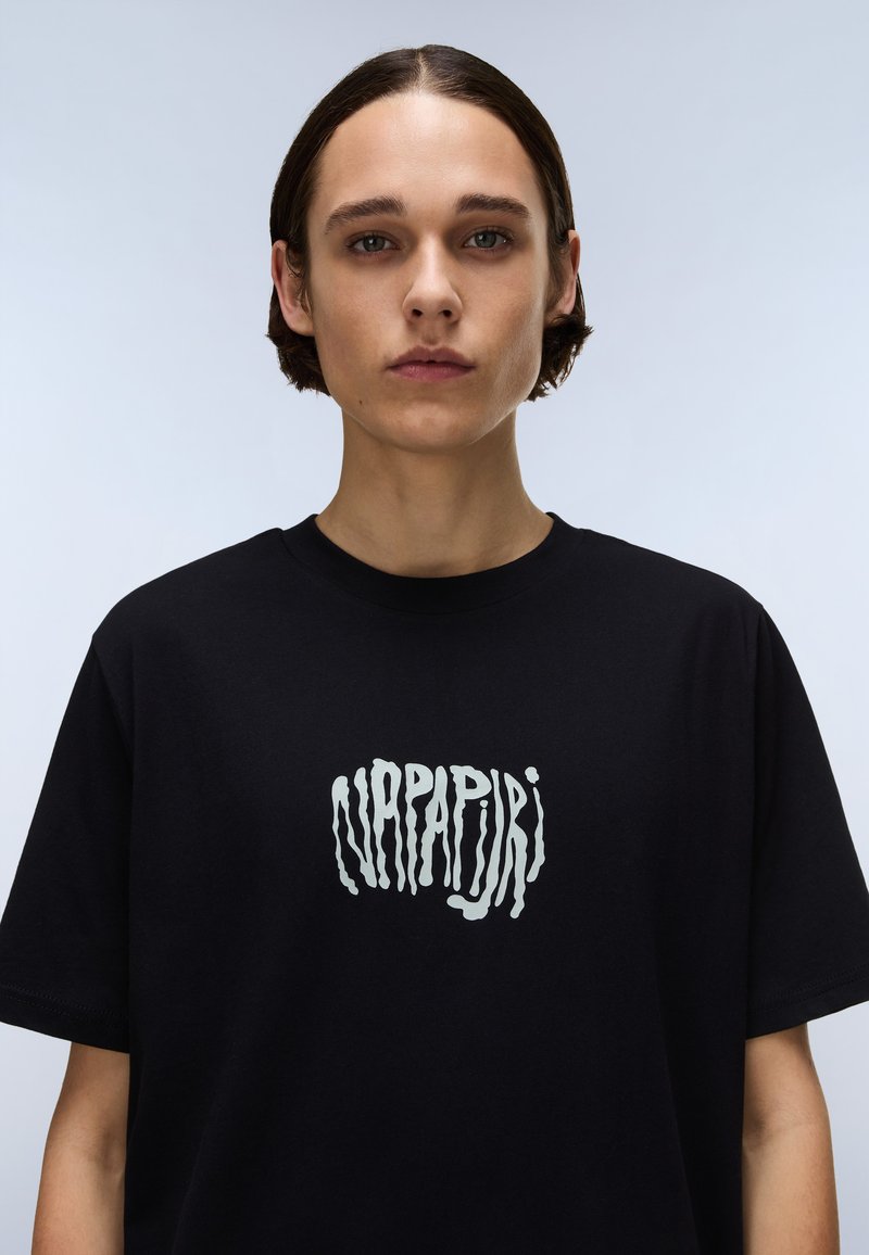 Camiseta de algodón negra con un logo blanco estilizado y prominente en la parte frontal. Cuello redondo clásico y mangas cortas.