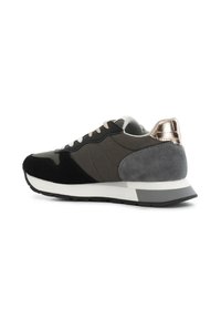 Baskets noires et grises avec un dessus en daim et en cuir lisse, accent métallique texturé au talon, semelle intermédiaire blanche et laçage à l'avant.