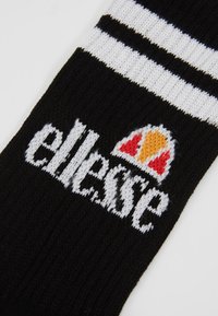 Calzino nero con righe bianche nella parte superiore, con un logo lavorato a maglia bianco di "ellesse" e un emblema rosso e giallo sopra il testo.