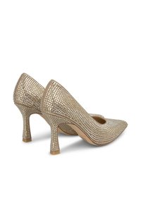 Le décolleté beige con tacco alto presentano un design in rete testurizzata decorato con piccoli borchie, punta affusolata e tacco sottile.