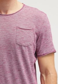 Lyhythihainen, pyöreäkaulainen t-paita teksturoidusta viininpunaisesta raitakankaasta, jossa on vasemmalla rintatasku ja litteät saumat.