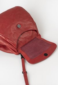 Rode leren rugzak met een opvouwbare klep met magneetsluiting, zachte suede interieurafwerking en een afneembare schouderband.