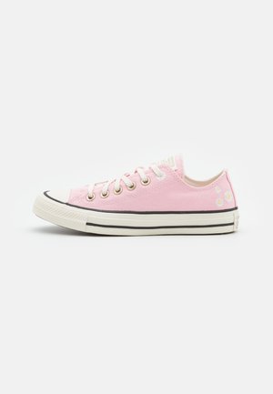 Low-top pink canvas sneaker with white rubber sole, lace-up front, and small white daisy embroidery on heel.