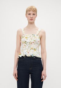 Blomstrete peplum-topp med hvit bakgrunn, med fargerike blomstermønstre, brede stropper og volangkant. Kombinert med mørke denimjeans.