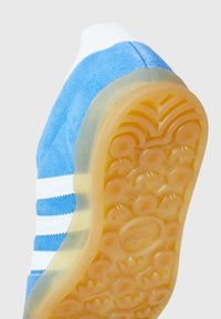 Blå mockasneakers med vita ränder, rund gummisula i genomskinlig gul färg, med mönstrad sula för bra grepp.