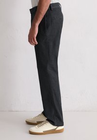 Ciemnoszare spodnie o prostym kroju nogawki z widocznym przeszyciem, w połączeniu z kremowymi trampkami, na jednolitym tle.