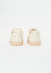 Krämfärgade sneakers med ovandel av texturerat läder, kontrasterande ljusrosa gummisula och präglad "GUESS"-logotyp på hälen.