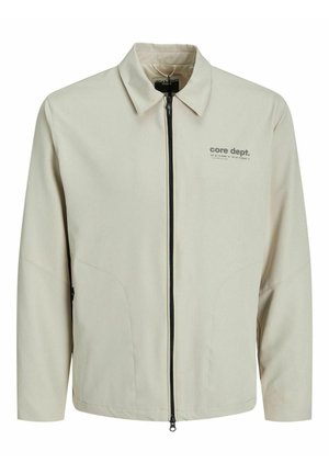 Beige színű, cipzáras dzseki hosszú ujjal, hegyes gallérral és két oldalsó zsebbel. Bal mellen logó található. Simaság jellemzi az anyag textúráját.