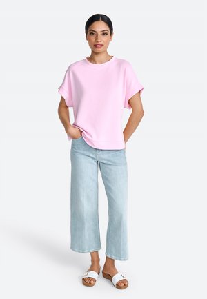 Sudadera de algodón rosa de gran tamaño, ajuste relajado, mangas cortas, combinada con jeans de pierna ancha de color azul claro y sandalias deslizantes blancas.