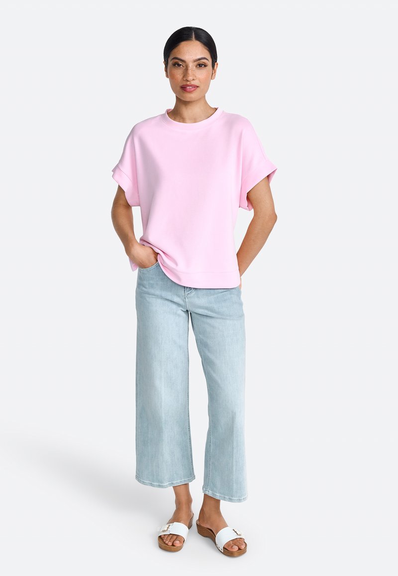 Sweatshirt en coton rose, coupe oversize, manches courtes, associé à un jean ample bleu clair et des sandales blanches à enfiler.