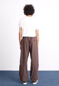 Bruna vida byxor med elastisk midja och bakficka, kombinerat med en enkel vit t-shirt med kort ärm och gröna sneakers.