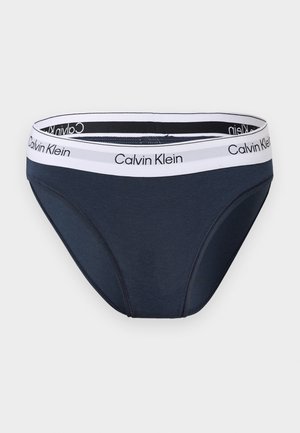 Caleçon slip homme bleu foncé avec ceinture élastique blanche portant le logo Calvin Klein noir.