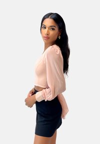Blouse courte rose clair avec manches longues bouffantes et texture lisse, associée à une mini jupe noire ajustée.