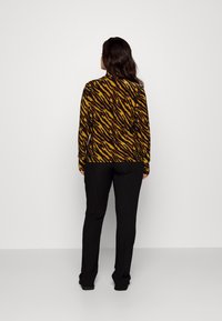 Langärmliges, Rollkragenoberteil mit einem Tigerstreifenmuster in Gelb und Schwarz, kombiniert mit schwarzen, gerippten, taillierten Hosen.