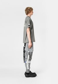 Camiseta gris de gran tamaño con mangas cortas, combinada con pantalones cargo grises que tienen múltiples bolsillos y correas, y zuecos negros texturizados.