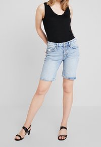 Shorts en jean bleu clair avec une coupe décontractée, conception à cinq poches et braguette à boutons, assortis à un débardeur noir et des talons noirs.