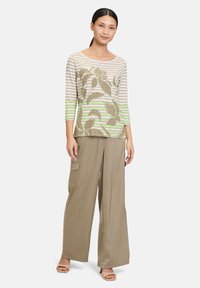 Gestreiftes Langarmoberteil mit olivgrünen und beigen Tönen, das ein Blättermuster aufweist. Locker sitzende beige weite Hosen mit seitlichen Taschen.