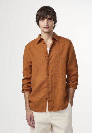 Camicia di lino color ruggine con bottone frontale, maniche lunghe arrotolate e una tasca a toppa singola. Tessuto leggermente testurizzato.