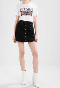 Camiseta blanca con texto gráfico negro y diseño de rosa, combinada con una falda de mezclilla negra de tiro alto con botones en la parte frontal. Botas blancas de tacón.
