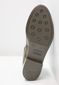 Suela de una bota impermeable marrón con clavos de tracción redondos, talla 37, y "Hecho en Portugal" grabado en la zona del talón.