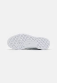 Bijela đon na tenisicama s teksturiranim gumenim uzorkom, kružnim logotipom i jasno vidljivim Reebok brendingom sa strane.