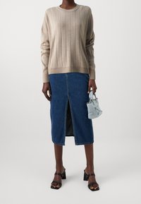 Beige ribbed knit neulepusero, farkku midi-hame, jossa on etuaukko, kevyen sinisen käsilaukun kanssa, jossa on koristeita, ja mustat paksupohjaiset sandaalit.