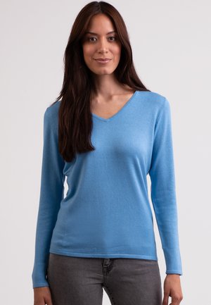 Blaues Langarm-V-Ausschnitt-Oberteil aus weichem Material, mit glatter Textur und entspanntem Schnitt. Kombiniert mit grauen Jeans.