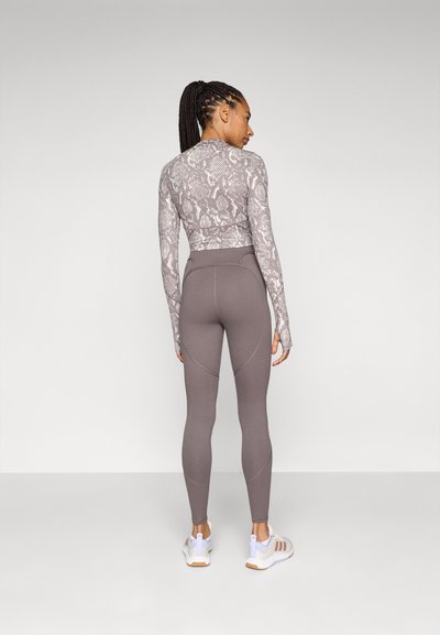 Woman with braided hair facing away, wearing a long-sleeve snakeskin top, high-waisted gray leggings, and white sneakers.
