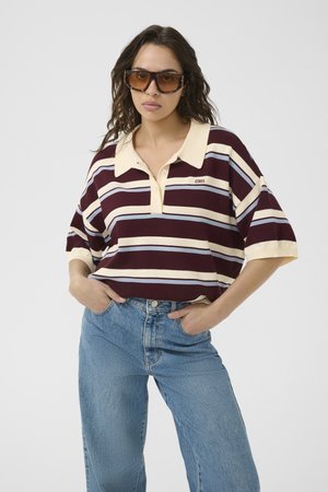 Maroon- und cremefarben gestreiftes Polohemd mit Kragen und drei Knöpfen, kombiniert mit hellblauen, hoch taillierten Jeans. Enthält große Sonnenbrille.