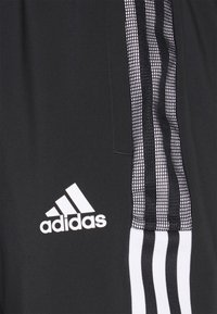 Svart tyg med vitt Adidas-logotyp och tre vita ränder kantade av ett svart nätmönster på höger sida.