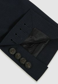 Manche de blazer bleu marine foncé avec quatre boutons noirs et boutonnières visibles, montrant une doublure intérieure noire lisse.