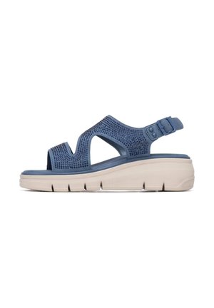 Sandalia azul de punta abierta con correa ajustable, diseño perforado con pequeños adornos y suela blanca gruesa con agarre texturizado.