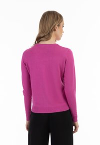 Pulover tricotat roz, bine ajustat, cu mâneci lungi, guler și tiv fixat, textură netedă și design minimalist. Vedere din spate.