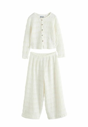 Biały dwuczęściowy zestaw o fakturowanej strukturze, składający się z krótkiego topu na guziki z długim rękawem oraz spodni o szerokich nogawkach, wykonany z lekkiego materiału.