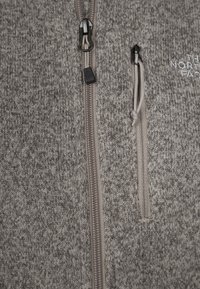 Grijze gebreide fleece met ritssluiting en een gladde textuur, met een contrasterende rits en een klein logo geborduurd op de borst.