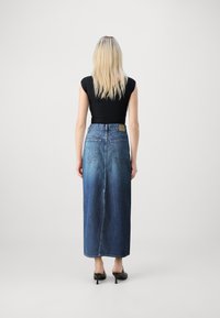 Gradient kék farmer maxi szoknya, magas derekú, hátsó zsebekkel. Fekete, testhez simuló felsővel és fekete magassarkú cipővel viselve.