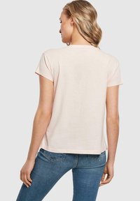 Kortærmet, lyserød t-shirt med rund hals. Blødt stof og afslappet pasform, lidt længere bagtil, syede kanter.