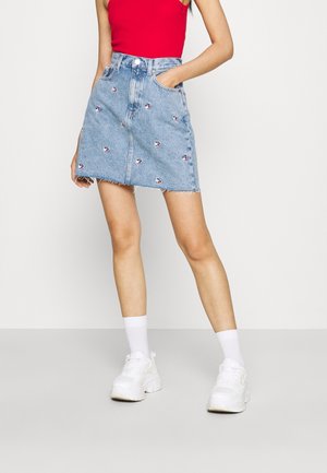 Denim miniskørt med en flosset kant, lyseblå farve, broderede detaljer og sidelommer, parret med en rød top og hvide sneakers.