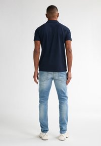 Polo shirt blu Navy a maniche corte, abbinato a jeans azzurri chiari. I jeans presentano una finitura sbiadita e tasche posteriori standard. Sneakers bianche.