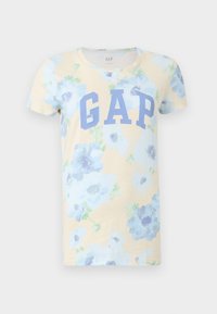 Camiseta beige de manga corta con estampado floral azul y gran texto azul "GAP" en el frente