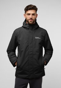 Zwarte waterdichte jas met capuchon, voorzien van een voorrits, twee zijzakken en het "Jack Wolfskin" logo op de borst.