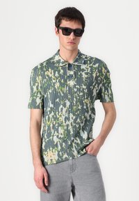 Kortermet polo shirt i et blått og grønt blomstermønster, med vertikale legg, spiss krage og knappelukking.