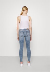 Jeans ajustados de cintura alta en azul claro, con un acabado desgastado, que cuentan con bolsillos traseros y una etiqueta de cuero marrón en la cinturilla.