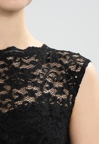 Haut en dentelle noire présentant des motifs floraux complexes, une texture transparente et des manches courtes, mettant en valeur un savoir-faire détaillé et un design sophistiqué.