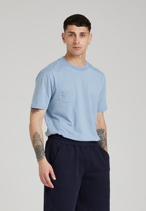 T-shirt in cotone azzurro chiaro con colletto rotondo e maniche corte, dotata di una tasca sul petto e logo ricamato. Abbinata a pantaloni corti scuri.