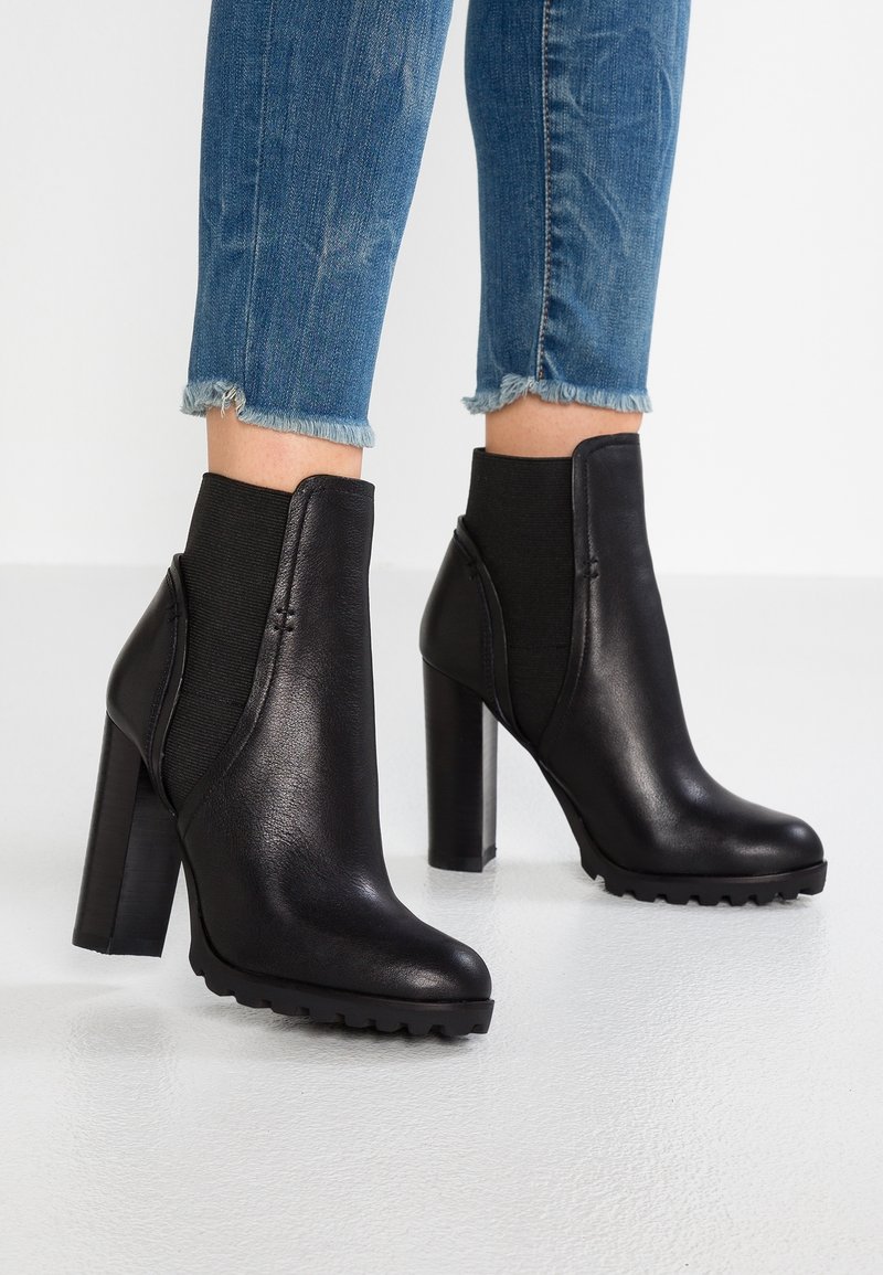 Bottines noires en cuir lisse, dotées de panneaux élastiques sur les côtés, d'un talon épais et d'une semelle texturée pour une meilleure adhérence.