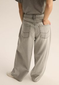 Szerokie, jasnoszare dżinsy z wysokim stanem, dwoma tylnymi kieszeniami i luźnym krojem. Tkanina ma miękką, lekko postrzępioną fakturę.