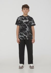 T-shirt nera con un motivo di marmo bianco e testo "TIMELESS". Abbinata a pantaloni neri e sneakers bianche con dettagli bordeaux.