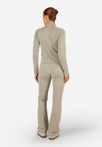 Bēša ribota adīta džemperis ar augstu apkakli, kombinēts ar saderīgiem platiem biksēm. Mīksta tekstūra, pieguļošs dizains un minimālistisks stils.