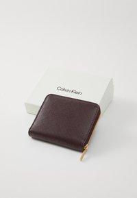 Calvin Klein burgundy wallet with a textured finish, gold zipper hardware, featuring a diamond pattern. Comes with a white branded box.